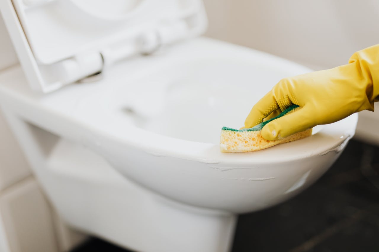 Crop unrecognizable person in yellow rubber glove cleaning toilet bowl with disinfecting detergent and sponge